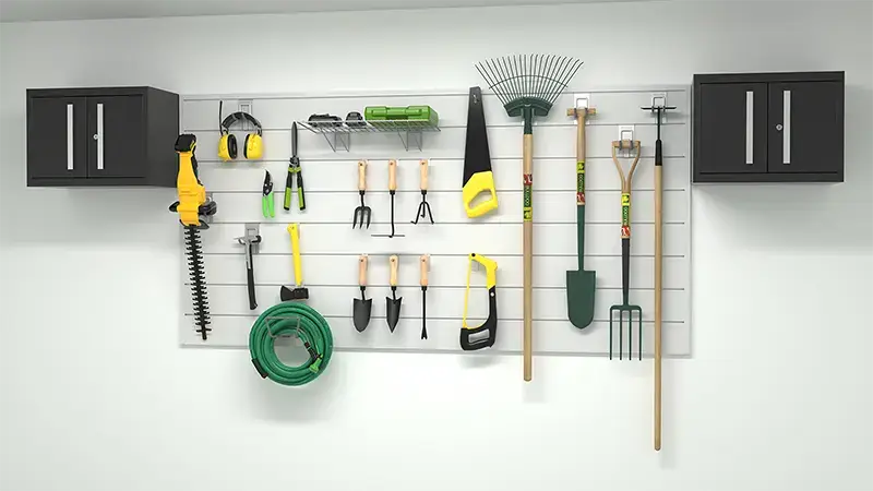 A neatly organized garage wall storage system displays various garden tools, including a hose, shears, rakes, a broom, trowels, a hedge trimmer, and a chainsaw. Two black storage cabinets are mounted above the pegboard holding the tools.