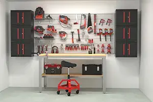 A well-organized garage workspace features a wooden workbench with a red and black mechanic's stool on wheels. The wall behind the bench displays an array of tools neatly arranged on a pegboard, and there are cabinets on either side for additional storage.