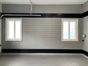 A clean, spacious garage interior with gray walls, black trim, two white-framed windows, a bare concrete floor, and a partially visible garage door mechanism at the top left. Perfect for anyone looking to reorganize their space or transform it into a functional workshop. This garage has no vehicles or items stored.