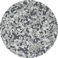 A circular sample of gray and white epoxy flooring with a flaked, terrazzo-style appearance. The pattern is composed of variously sized flakes in different shades of gray, white, and black, creating a textured and speckled surface.