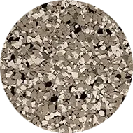 A circular image displaying a close-up of a surface covered with small, irregularly-shaped flakes in various shades of gray, beige, and black. The flakes are tightly packed, creating a textured, mosaic-like pattern.